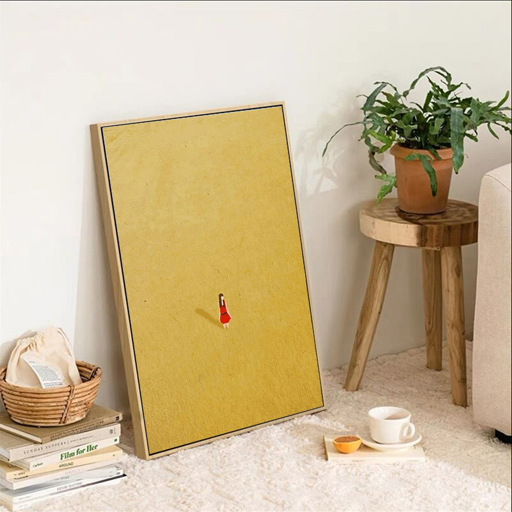 Yellow framed artwork with a red figure on a white wall, next to a plant and small table.