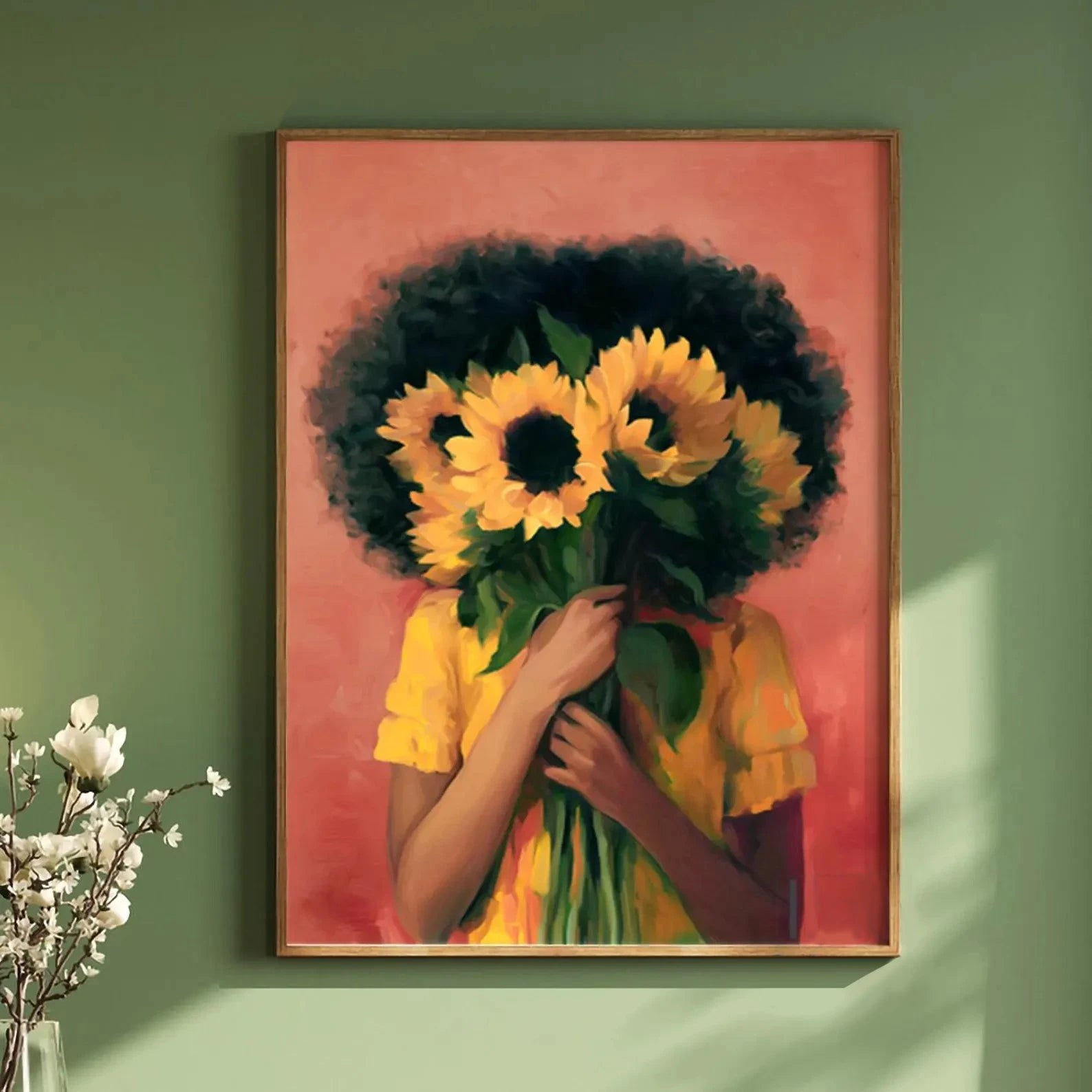 Framed artwork of a person with an afro holding sunflowers against a pink background, displayed on a green wall.