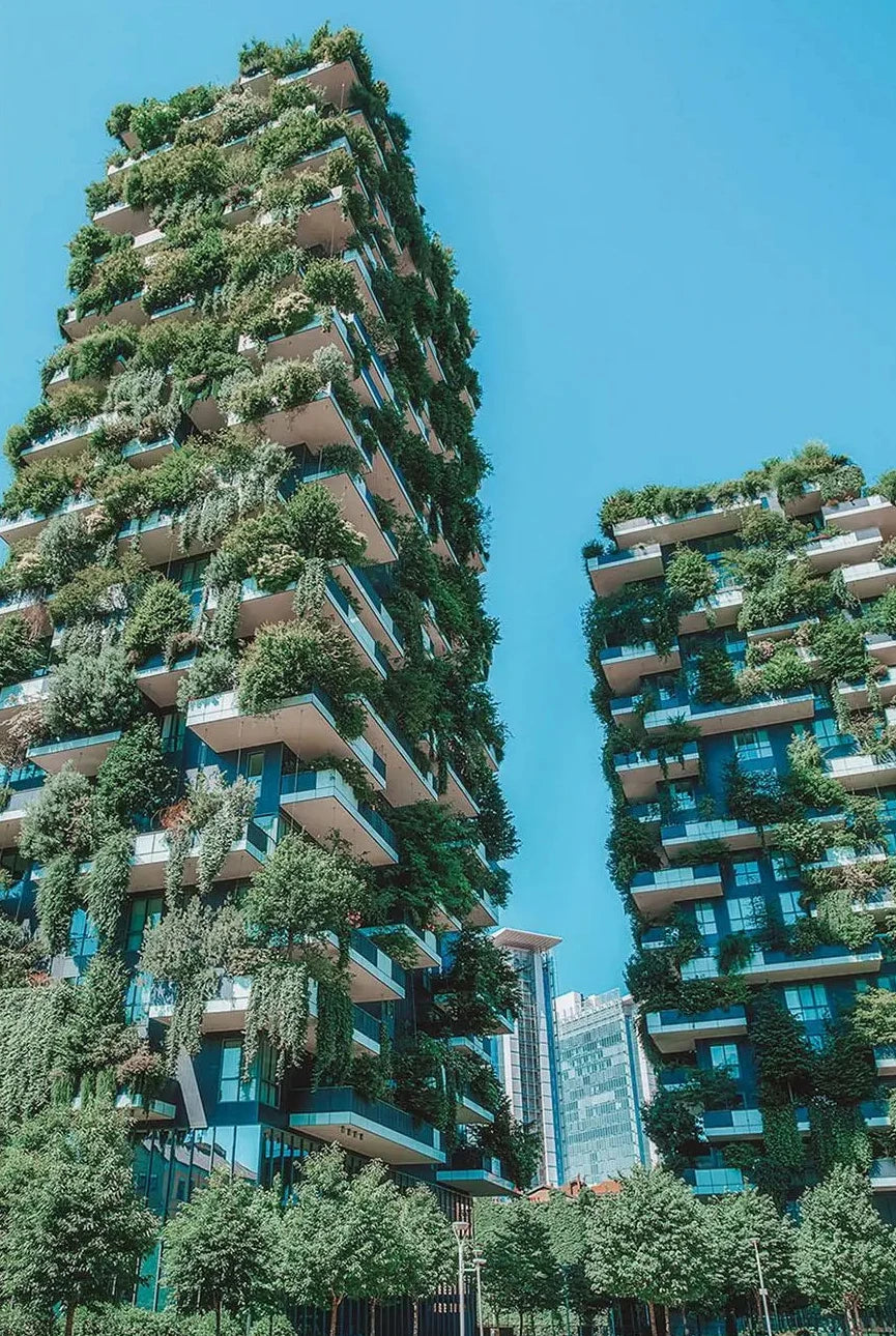 Tall buildings with extensive greenery on their facades against a clear blue sky.