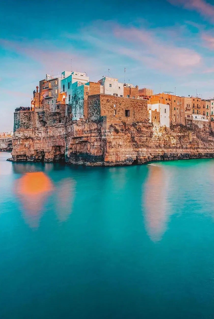 Cityscape with stone buildings on a cliff overlooking turquoise water
