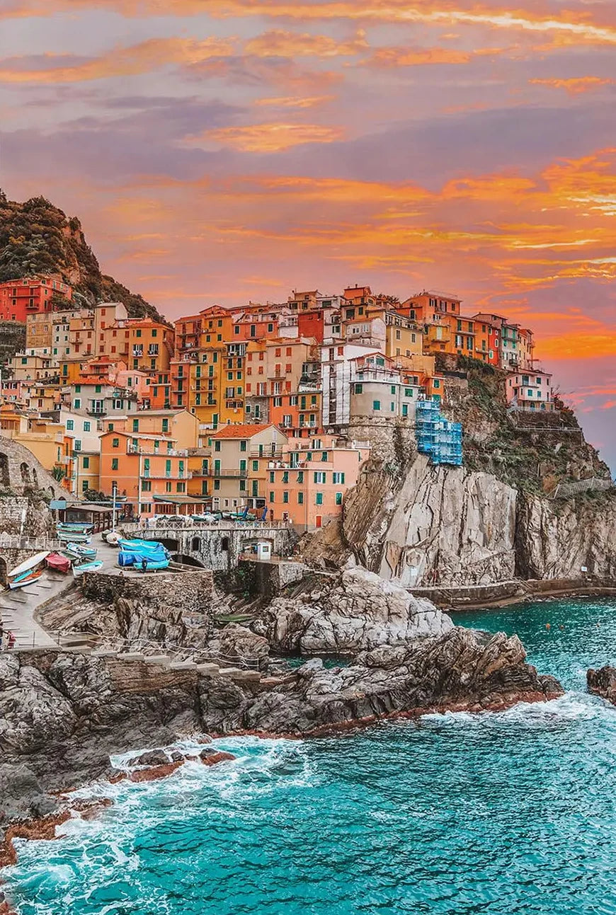 Colorful coastal town on a cliff with a vibrant sunset sky.