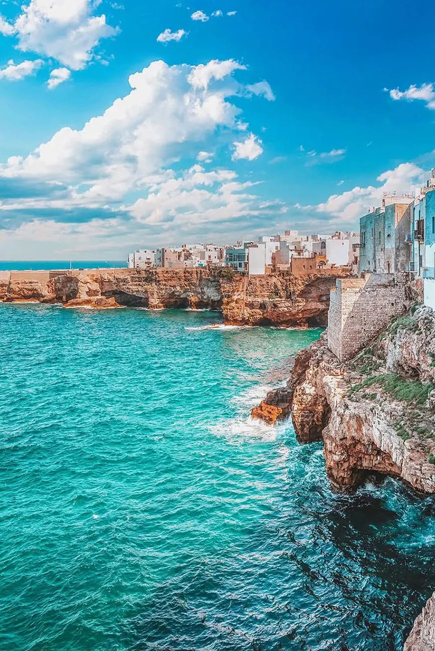 Coastal town with buildings built into cliffs overlooking turquoise ocean and blue sky.