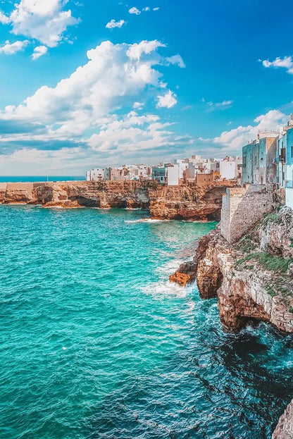 Coastal town with buildings built into cliffs overlooking turquoise ocean and blue sky.
