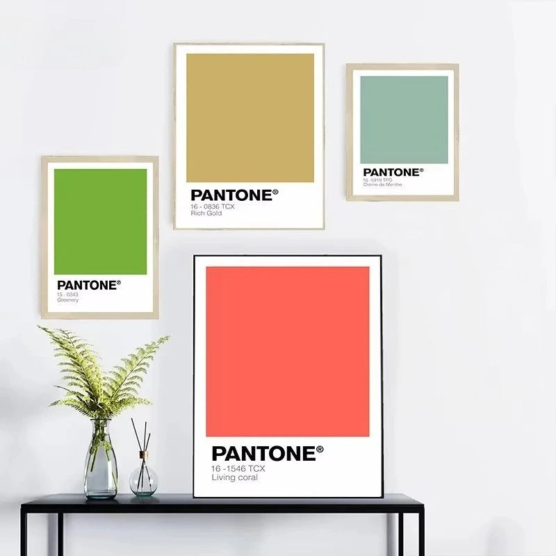 Four Pantone color posters on a wall with a black table and plants.
