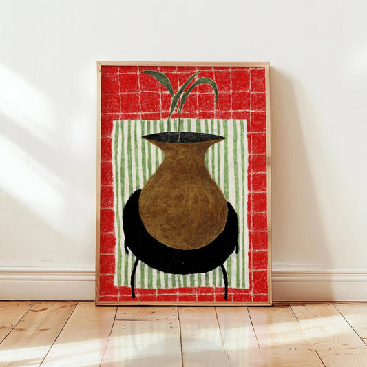 Framed artwork of a vase with a plant on a red and green striped background, leaning against a white wall. Canvas & Curio