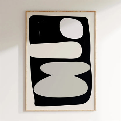 Framed abstract art print with black, white, and gray shapes on a white wall.