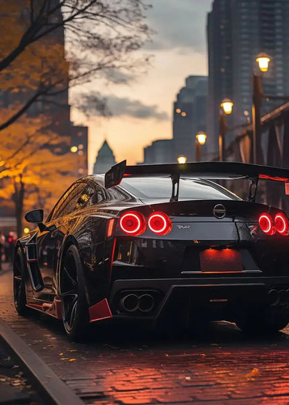 Black sports car with red taillights on a city street at sunset.