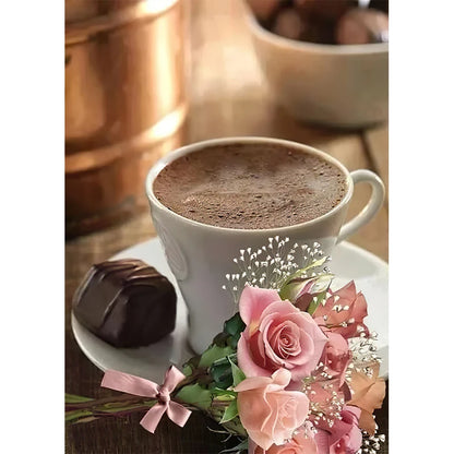 White mug of hot chocolate with a pink rose and chocolate truffle on a wooden table.