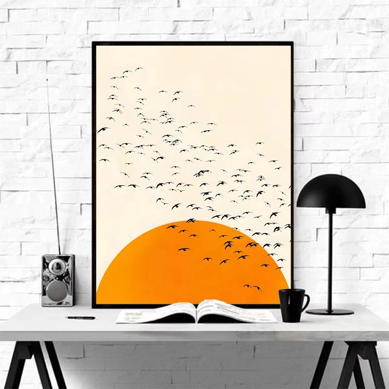 Framed artwork of birds flying over an orange sunset on a white wall.