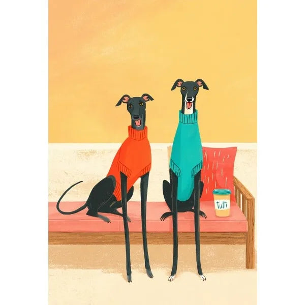 Two dogs wearing colorful sweaters sitting on a couch with a cup of coffee.