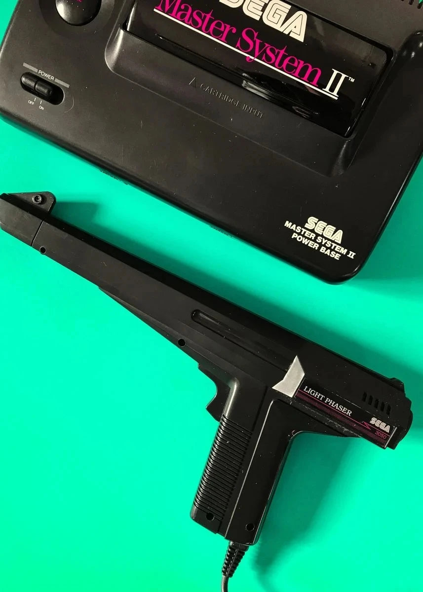 Sega Master System II console and light Phaser on a teal background