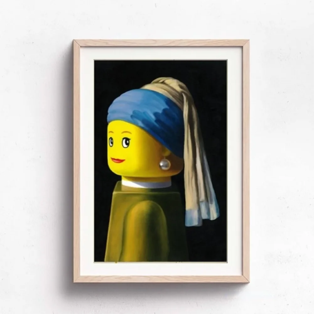 Framed artwork of a LEGO figure with a pearl earring on a white wall.