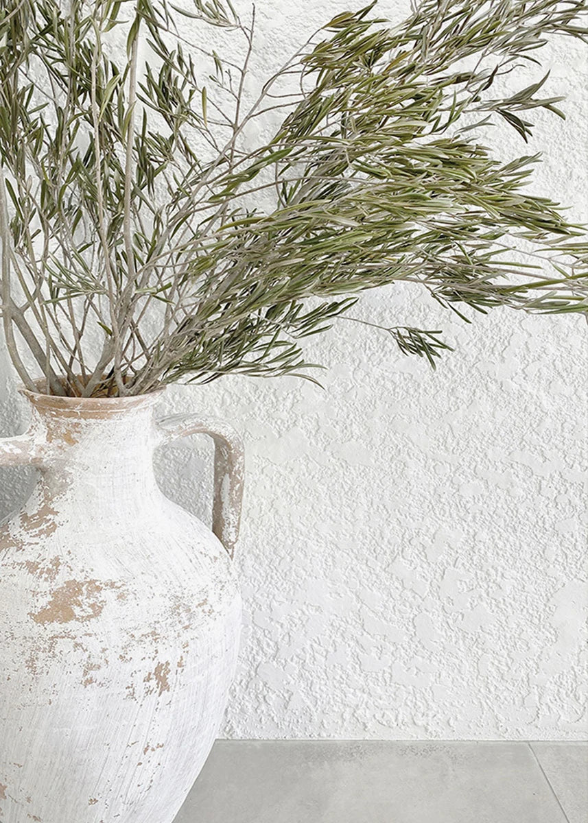 White textured wall with a distressed ceramic vase holding green branches.