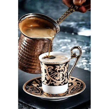 Copper pot pouring coffee into a decorative cup on a reflective surface