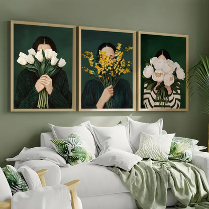 Three framed artworks of a person holding flowers above their face on a wall above a bed.