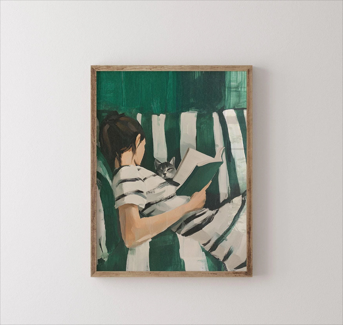 Framed artwork of a person reading a book with a cat on a striped blanket against a green background.