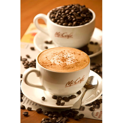 Two McCafe coffee cups with cappuccino and coffee beans on a wooden surface.