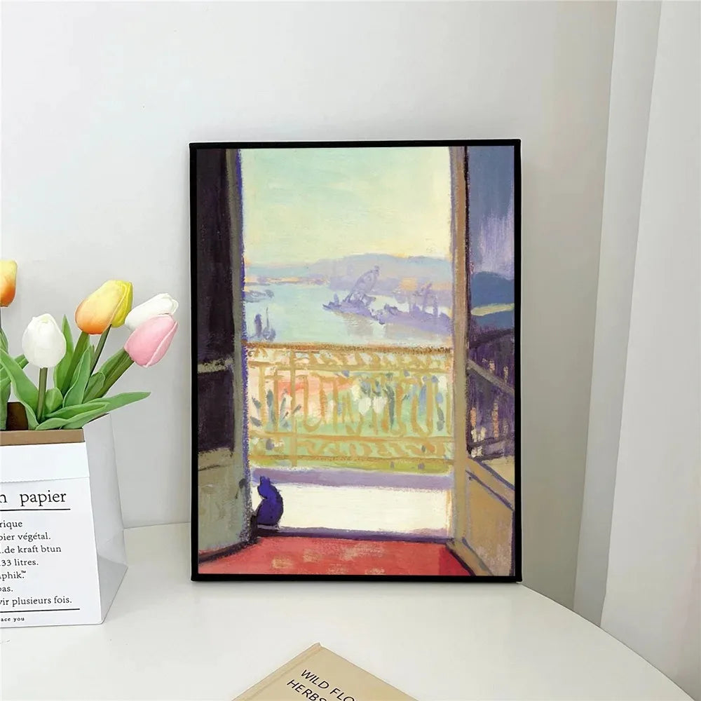 Framed artwork of a scenic view with a cat on a windowsill, placed on a white surface.