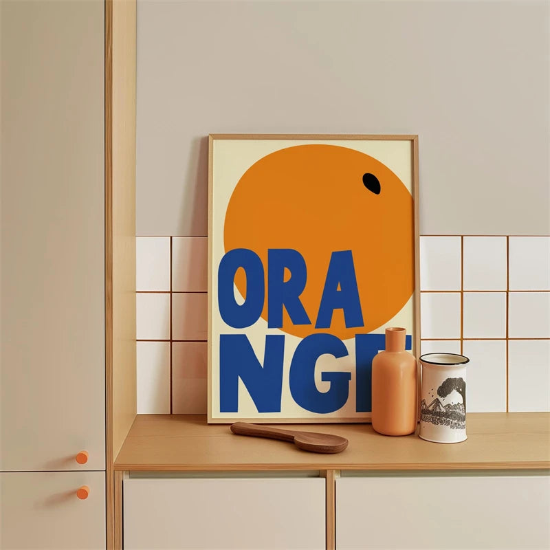 Framed artwork with 'ORANGE!' text on a kitchen counter with decorative items.