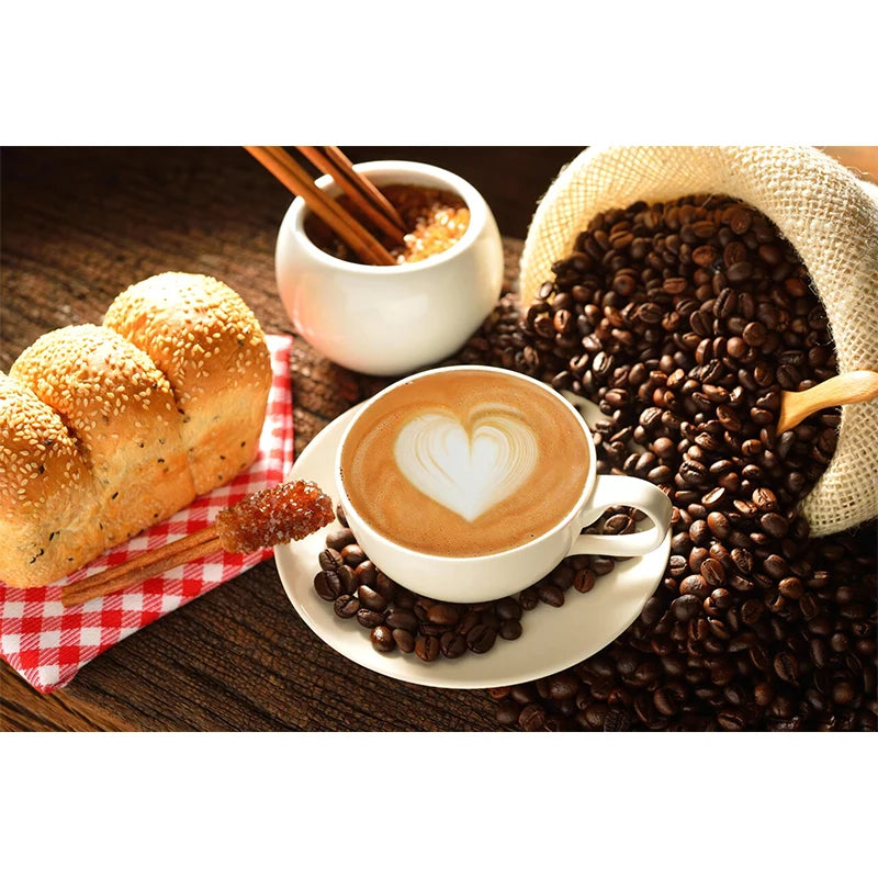 Cup of coffee with latte art, surrounded by coffee beans, bread, and a checkered cloth on a wooden table.