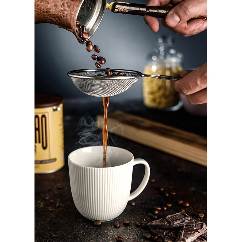Coffee being poured from a portafilter into a white mug with coffee beans and chocolate around.