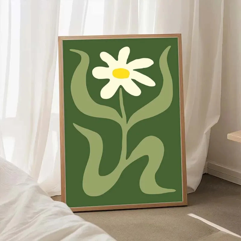 Framed artwork of a white flower with green leaves on a green background, placed indoors.