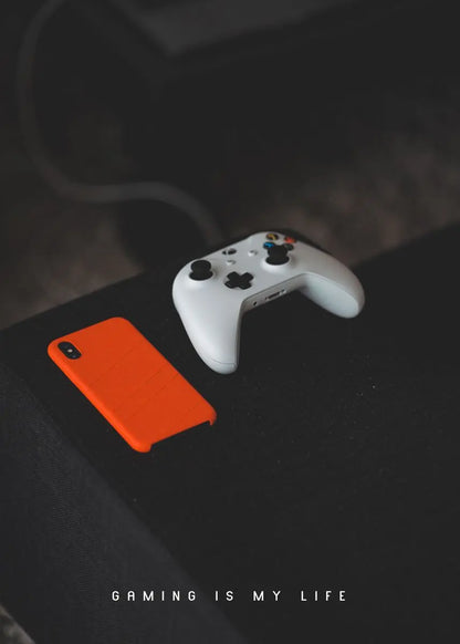 White gaming controller and orange phone case on a dark surface with 'Gaming is My Life' text.