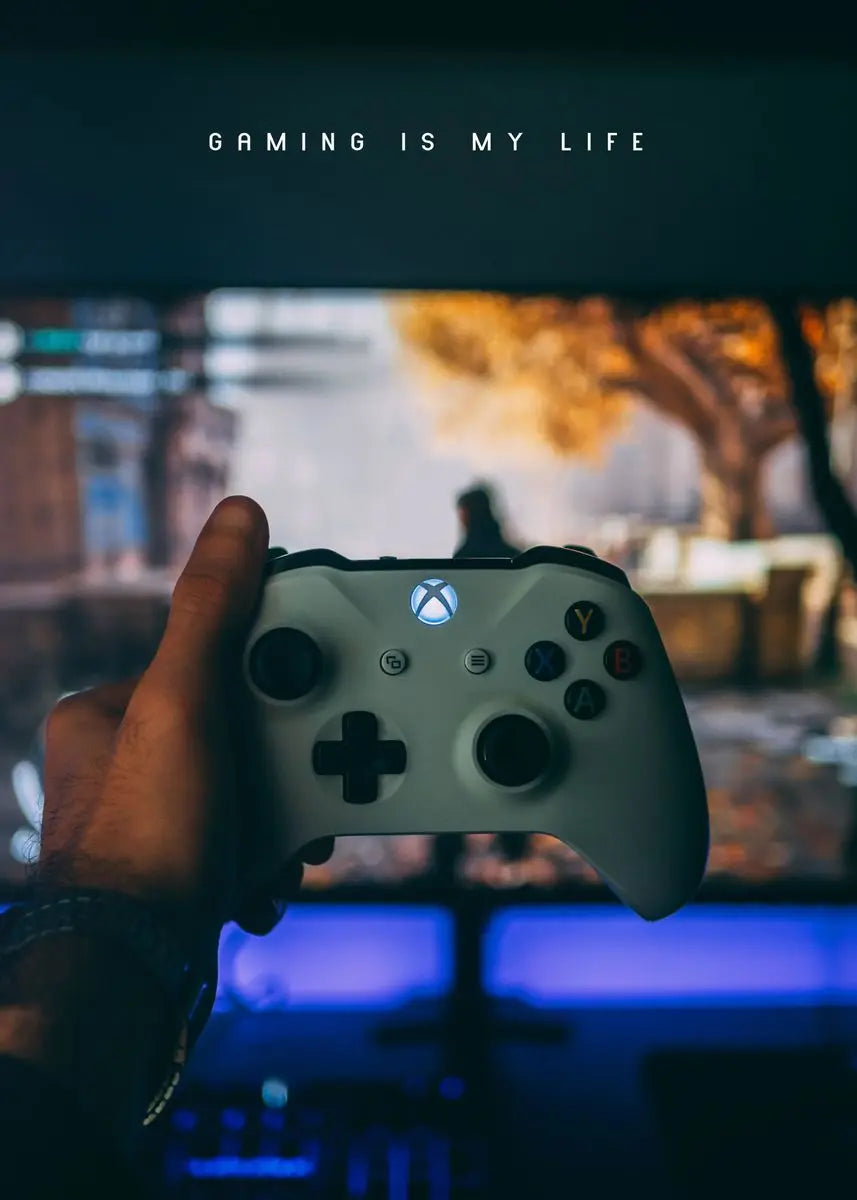 Hand holding a gaming controller with 'Gaming is my life' text above on a blurred gaming setup background.