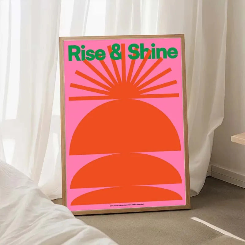 Poster with 'Rise & Shine' text and sun design on a pink background, leaning against a white curtain.
