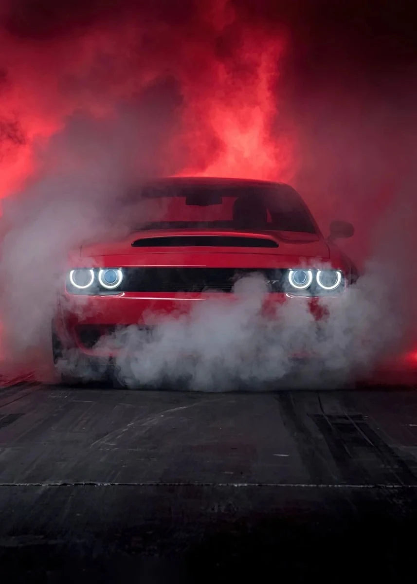 Red car with glowing headlights amidst red and white smoke in a dark setting