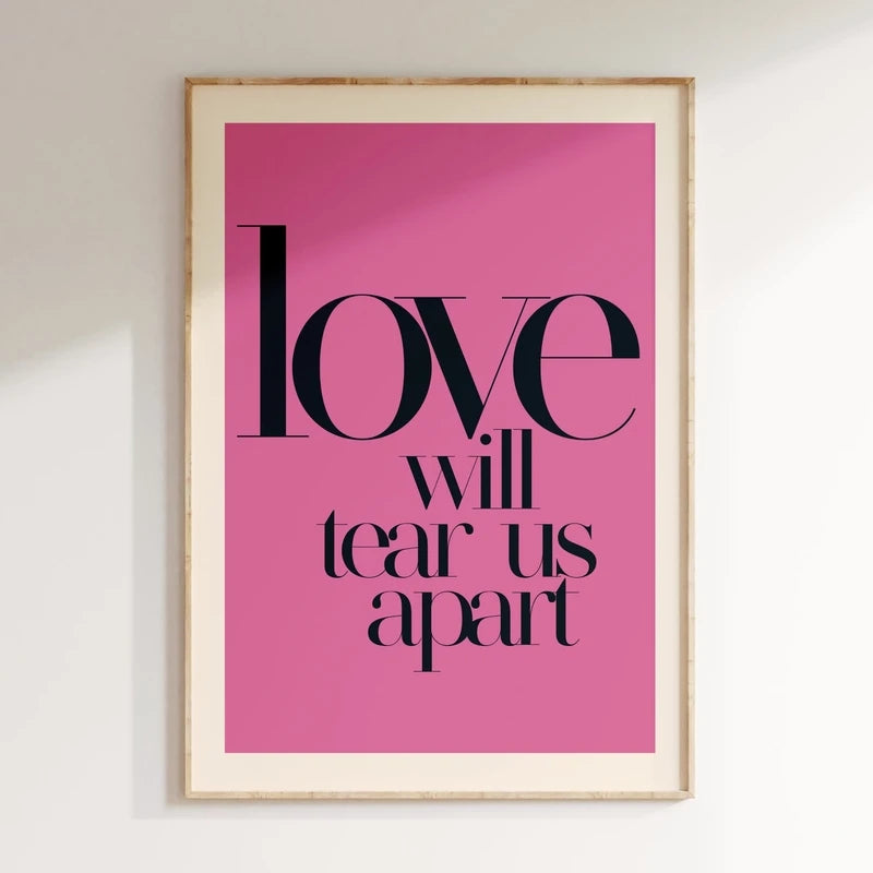 Framed pink poster with black text 'love will tear us apart' on a white wall.