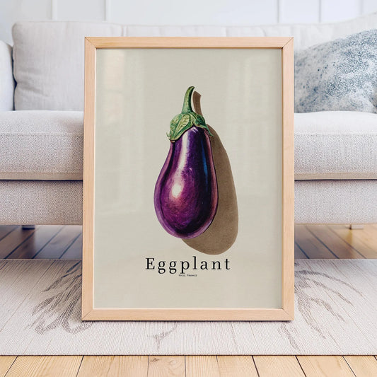 Framed print of an eggplant on a light background, displayed in a room with a couch. Canvas & Curio