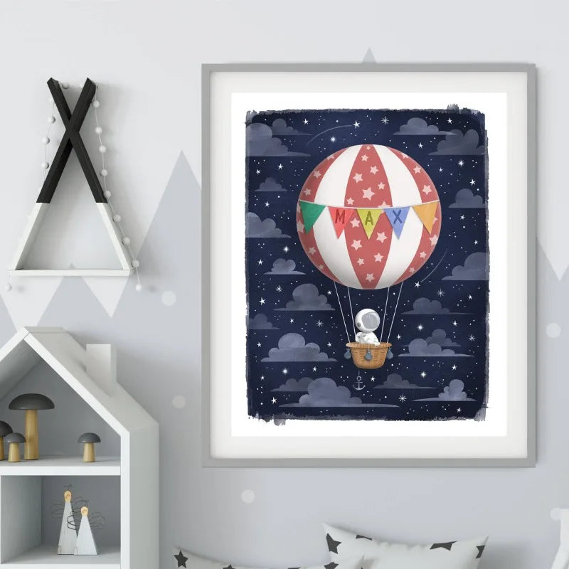 Framed artwork of a hot air balloon with colorful flags against a starry night sky, displayed on a wall.