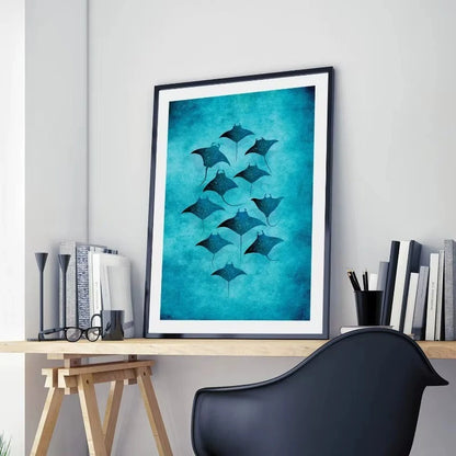 Framed artwork of manta rays on a teal background above a desk with books and a chair.